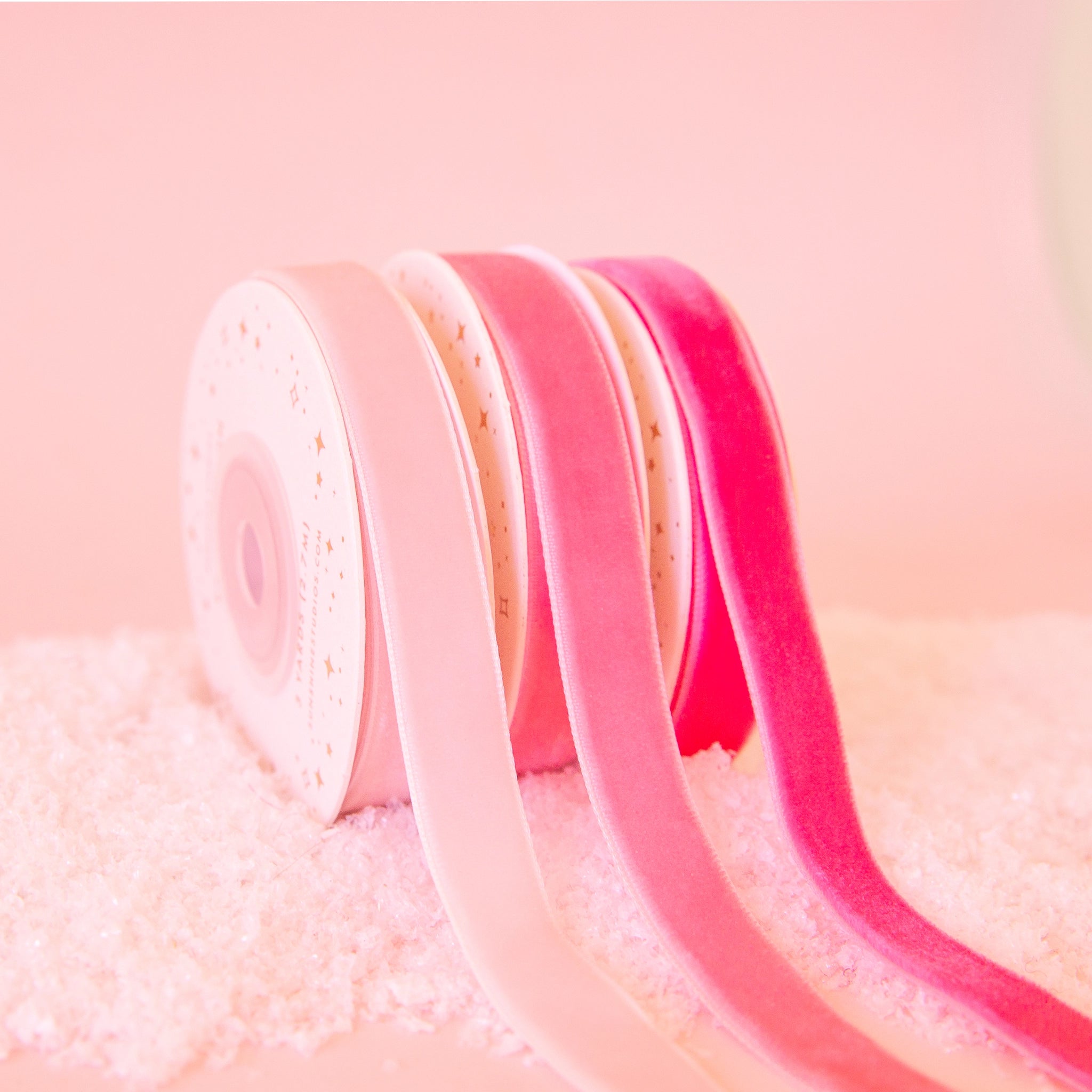 On a pink background is the three spools of velvet ribbon in three different shades of pink.