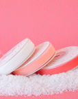 On a pink background is three spools of velvet ribbon in three different shades ranging from white to a peachy pink.