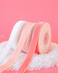 On a pink background is three spools of velvet ribbon in three shades. From left to right the colors are white, light pink and peach.