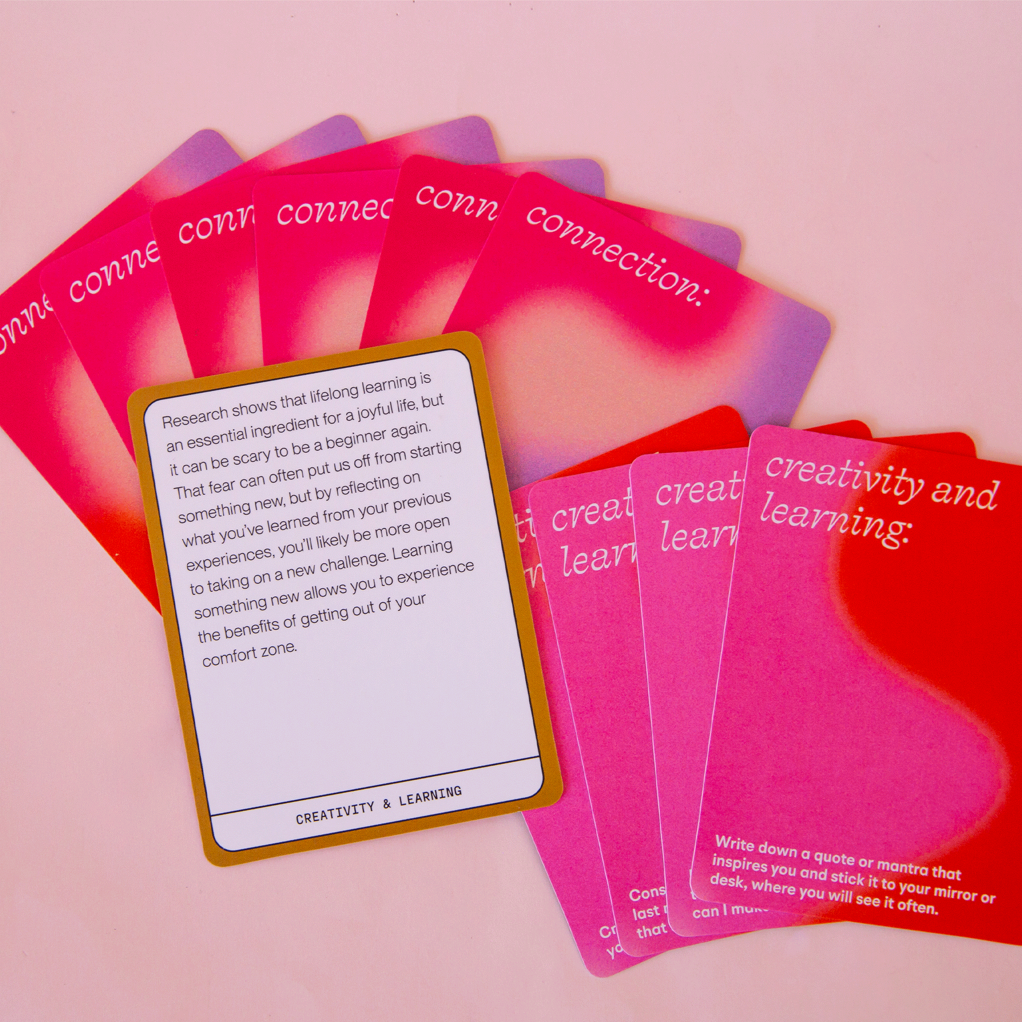 On a pink background is a deck of cards with inspirational quotes on one side and a wavy colorful design on the other. 