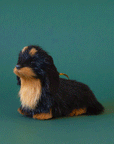 On a green background is a furry black and tan dachshund shaped ornament.