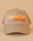 On a tan background is a tan trucker hat with yellow and orange gradient text that reads, "California".