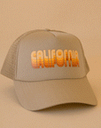 On a tan background is a tan trucker hat with yellow and orange gradient text that reads, "California".