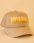 On a tan background is a tan trucker hat with yellow and orange gradient text that reads, "San Diego".
