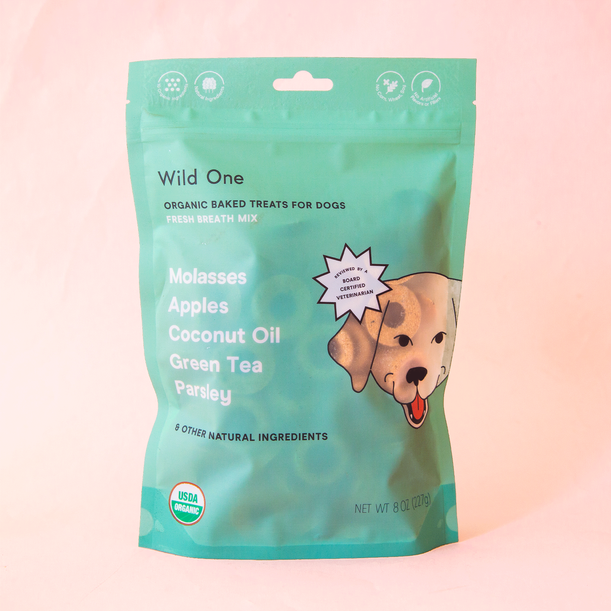 On a peach background is a green bag of dog treats with a dog graphic and text that reads, &quot;Wild One Organic Baked Treats For Dogs&quot;.