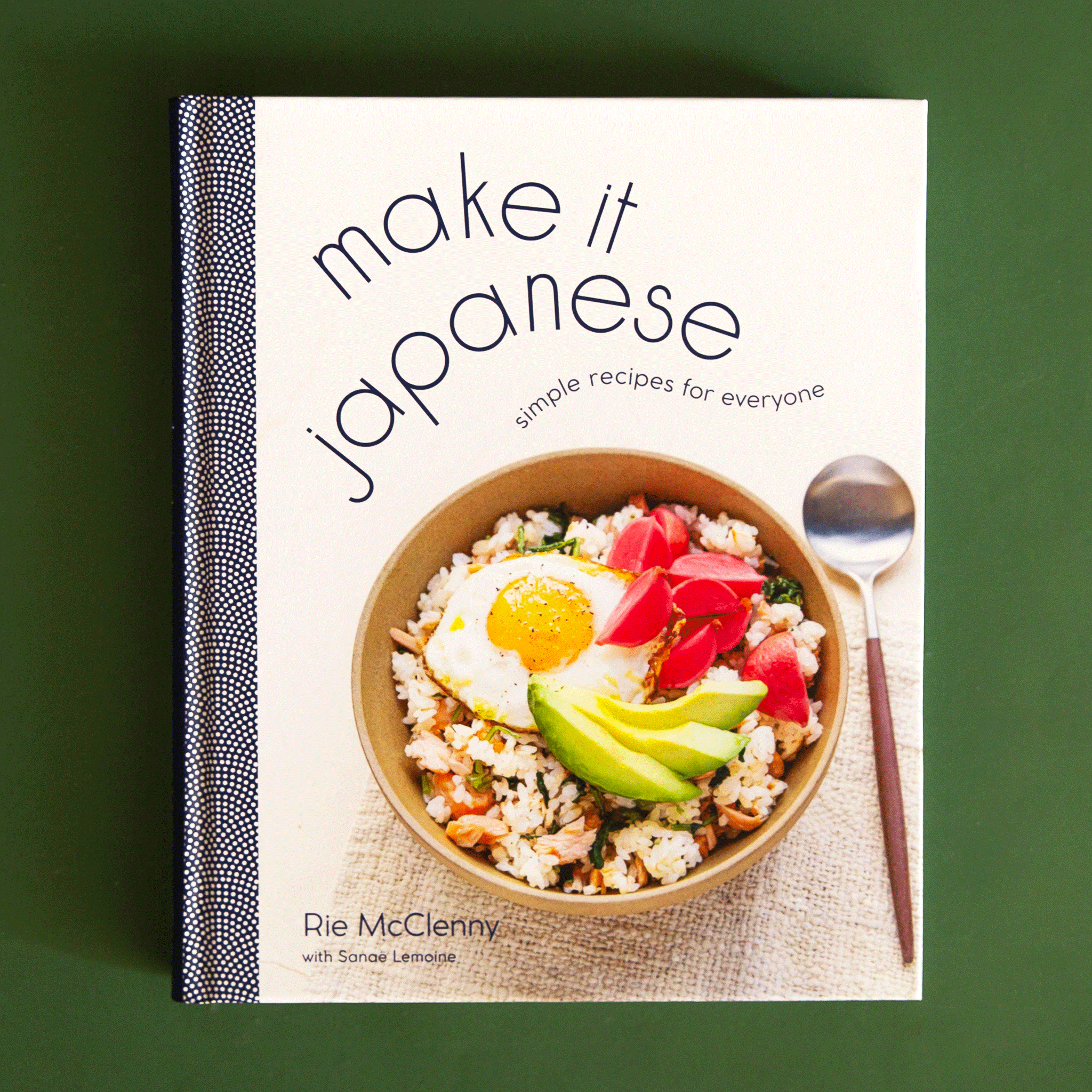 On a green background is an ivory book cover with a book of food and wavy text above it that reads, "make it japanese simple recipes for everyone".