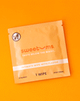 On an orange background is an orange packet of a single use feminine wipe.
