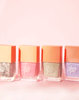 On a pink background is four rectangle bottles of nail polish next to one another. There is a silver sparkle, light pink, sage green and lilac purple color.