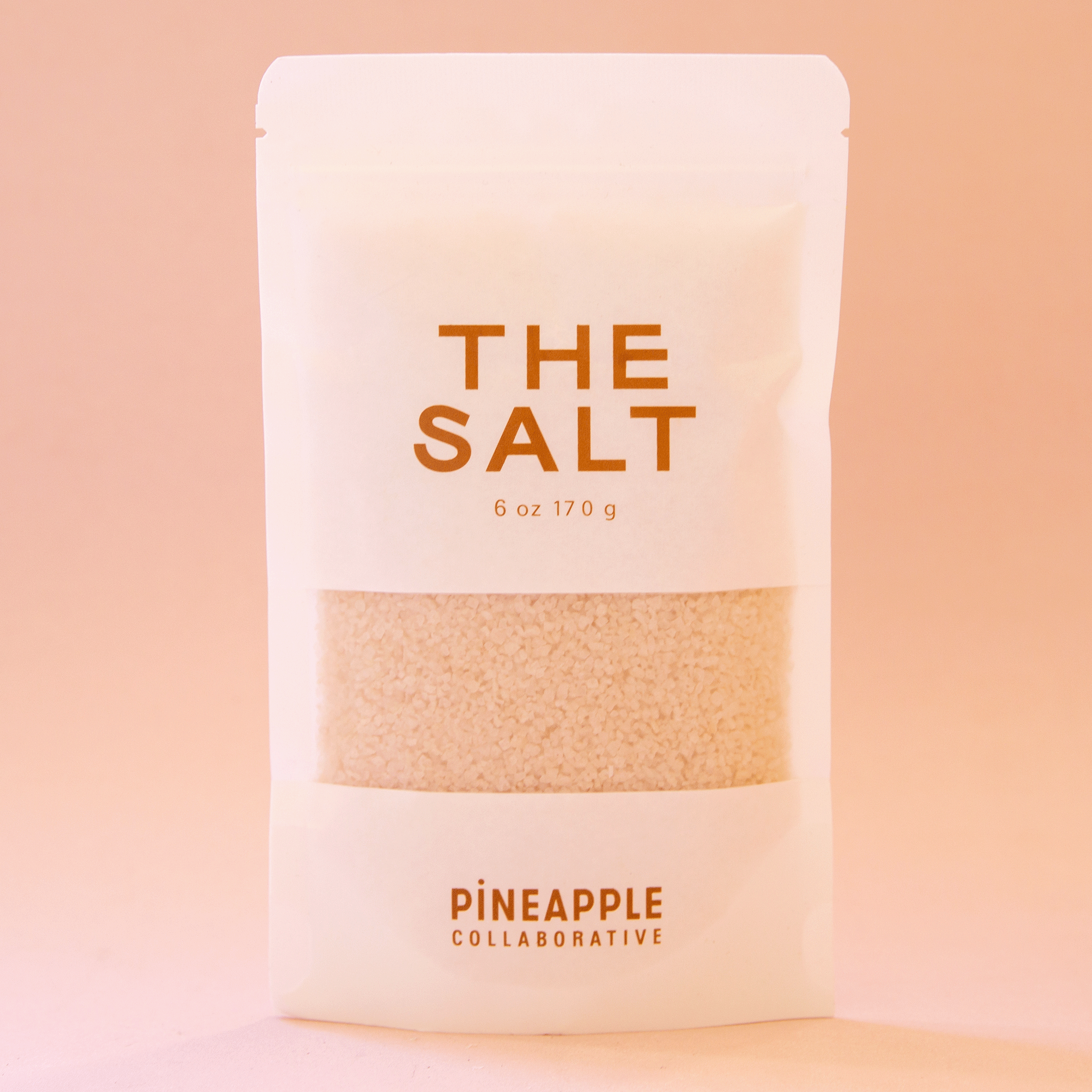 On a peachy background is a white bag of pink salt with brown text that reads, "The Salt".
