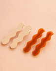 On a peach background is two pairs of wavy hair clips.