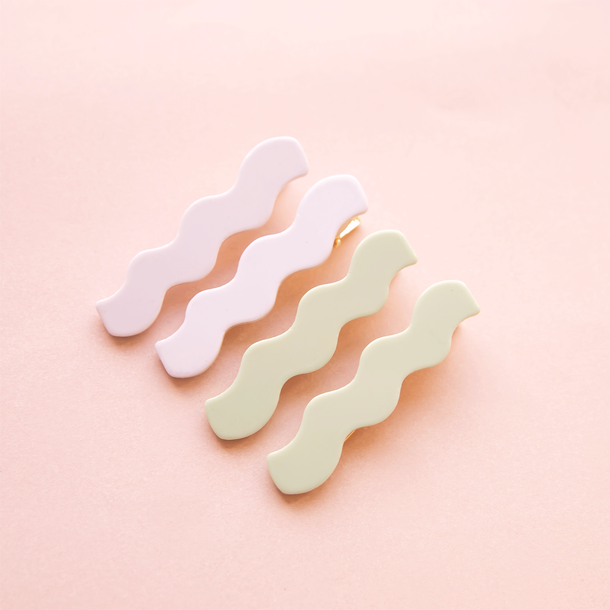 On a pink background is two sets of wavy shaped hair clips in a light green/blue shade and shade of white.