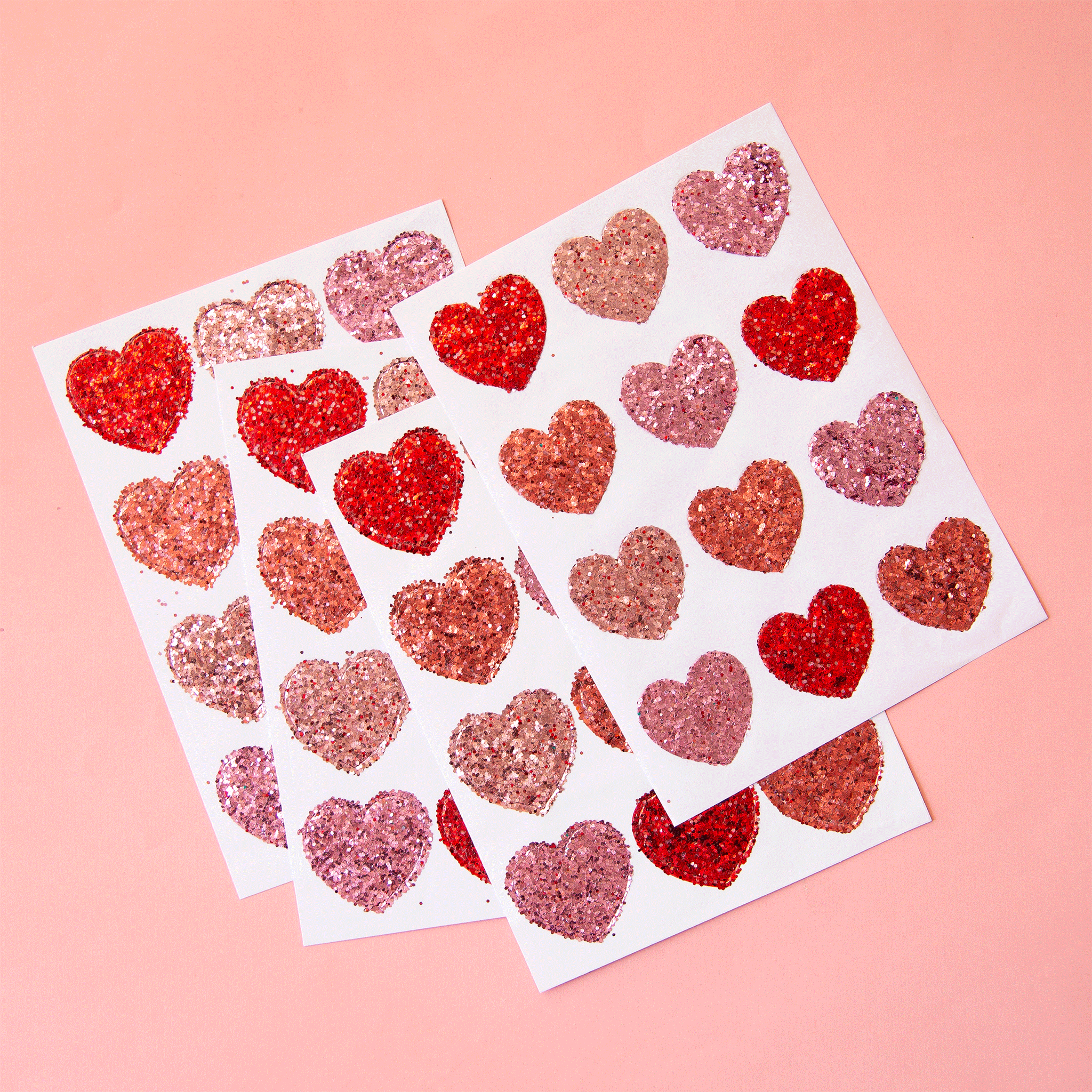 On a pink background is four sheets of heart shaped glitter stickers in shades of red and pink.  Edit alt text