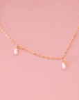 A dainty gold chain necklace with five freshwater pearls hanging spaced out on the chain.