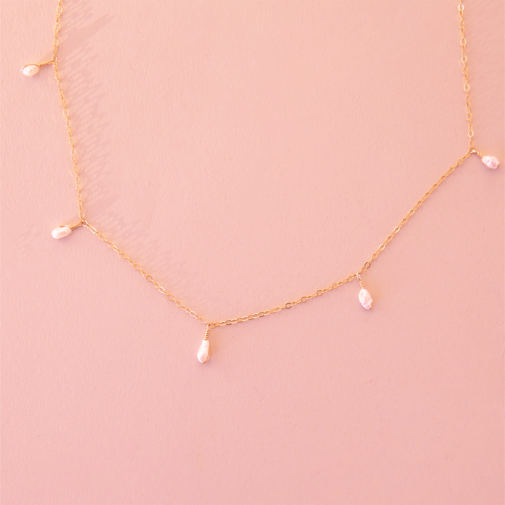 A dainty gold chain necklace with five freshwater pearls hanging spaced out on the chain.