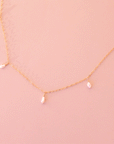 A dainty gold chain necklace with five freshwater pearls hanging spaced out on the chain.