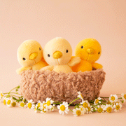 On a pink background is three chick stuffed animals in a fuzzy nest surrounded by tiny daisies not included with purchase. 