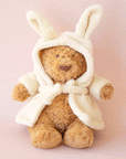 On a pink background is a brown stuffed animal bear wearing a fuzzy white rope with bunny ears.