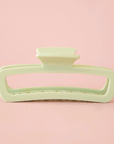 On a pink background is a rounded rectangle hair claw clip in mint green shade.
