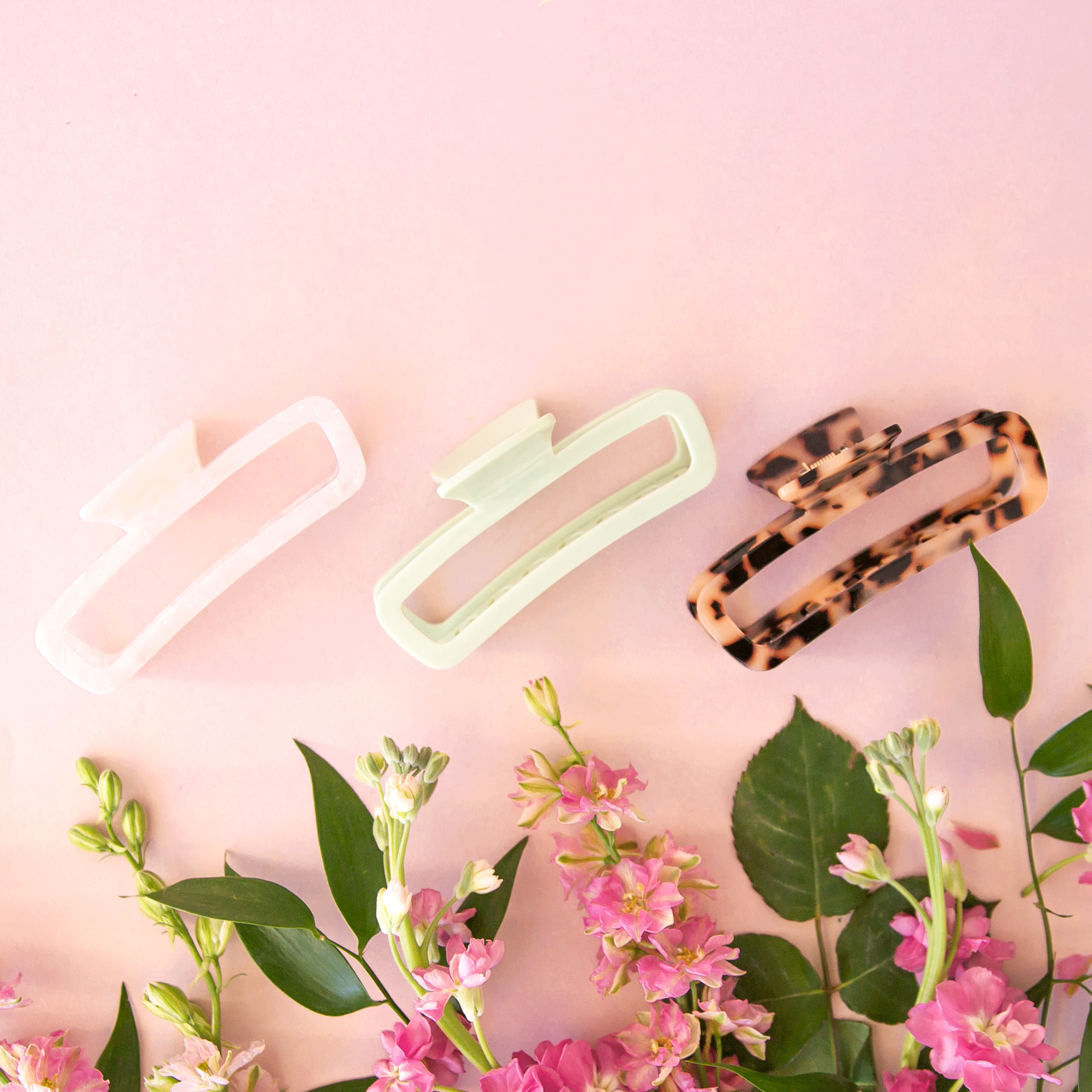 On a light pink background is three of the rectangle claw clips in a light tortoise shade, a pearly white and a light mint green. 