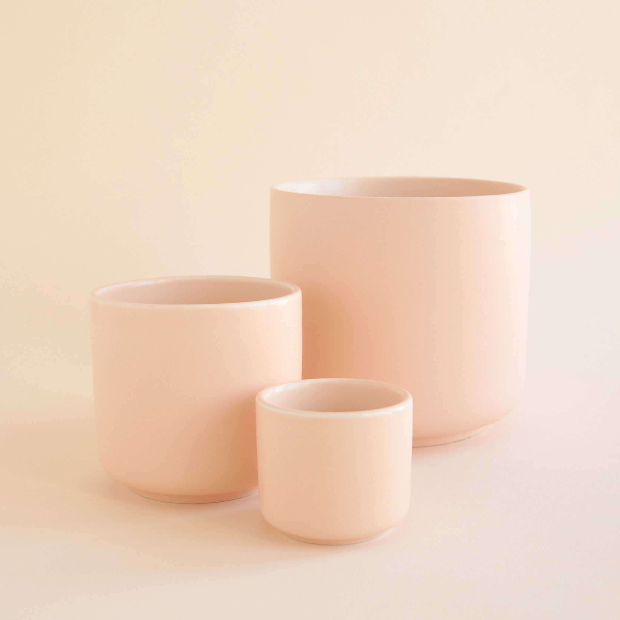On a cream background is three different sized pink ceramic pots.