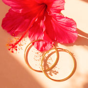 Gold hoops shown on a pink background with purple orchid flowers.