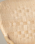 On an ivory background is a rattan chair with a woven rattan seat and backrest. This photo has a close up of the cane detailing.
