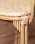On an ivory background is a rattan chair with a woven rattan seat and backrest. This photo shows the details of the cane detailing.