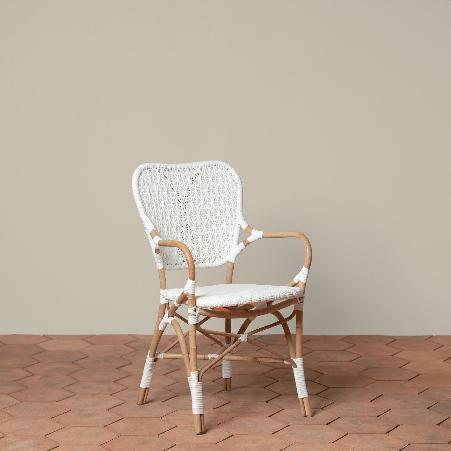 On a neutral background is a white and tan woven rattan chair with woven cane on the backrest and seat. 