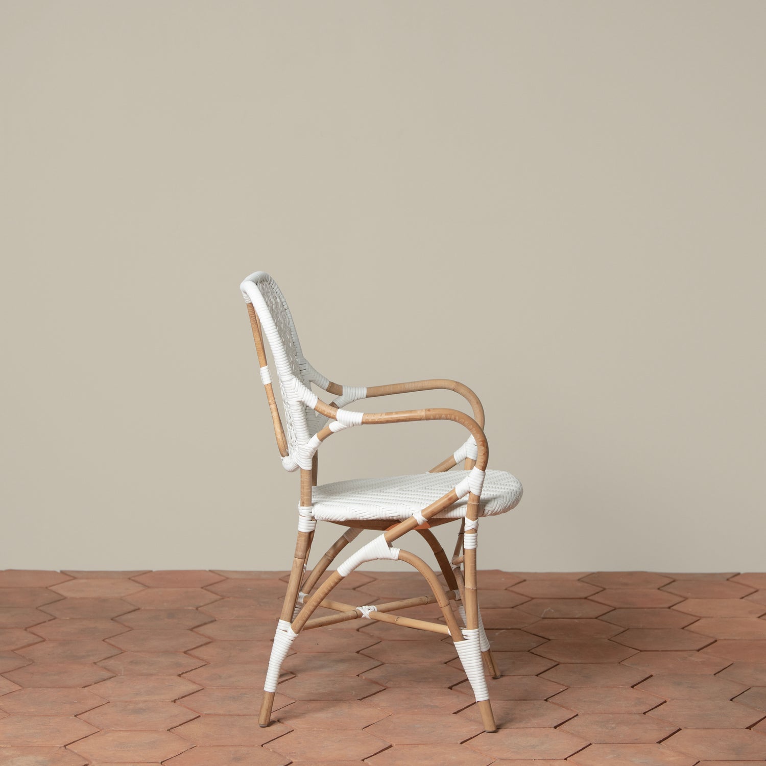 On a neutral background is a white and tan woven rattan chair with woven cane on the backrest and seat.