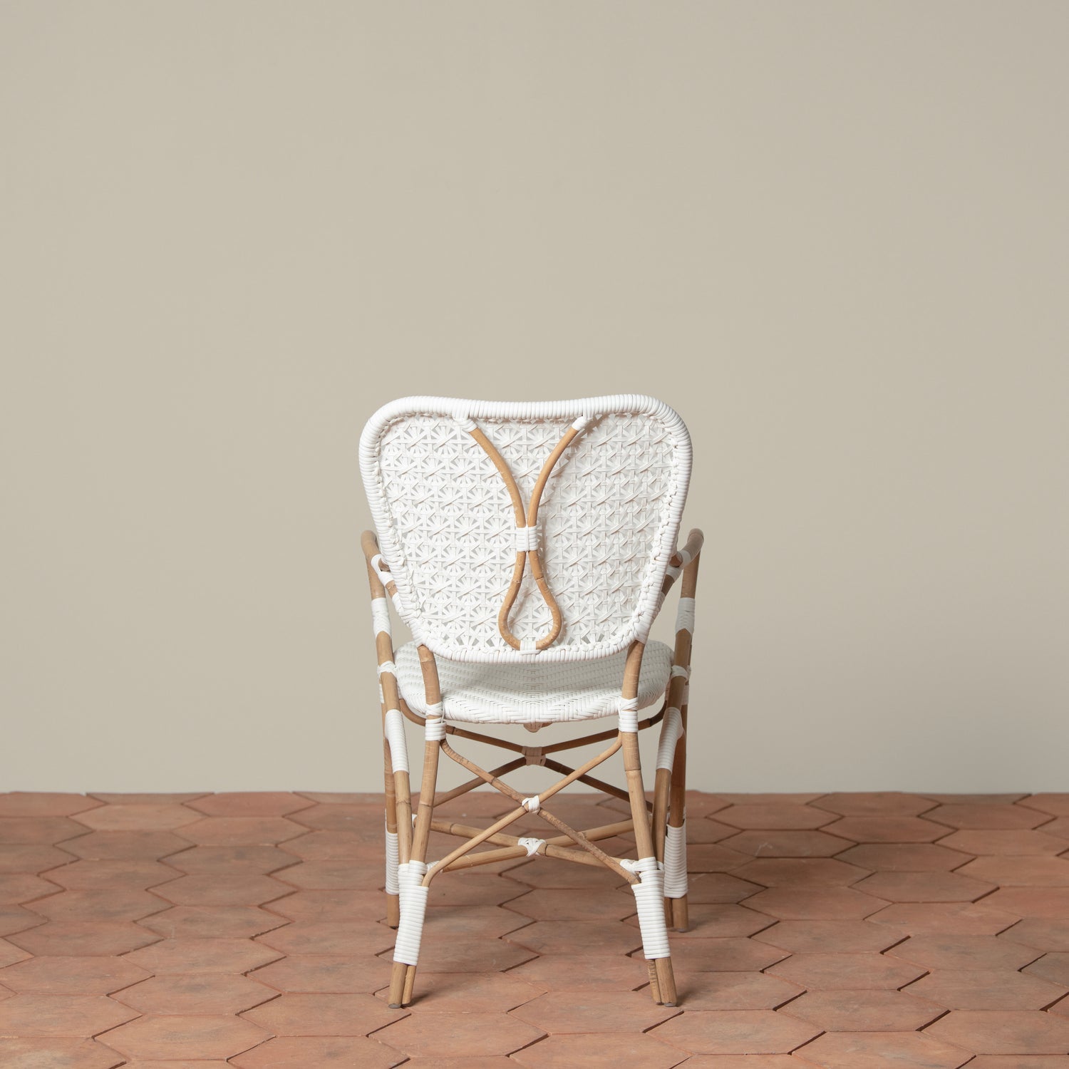 On a neutral background is a white and tan woven rattan chair with woven cane on the backrest and seat.