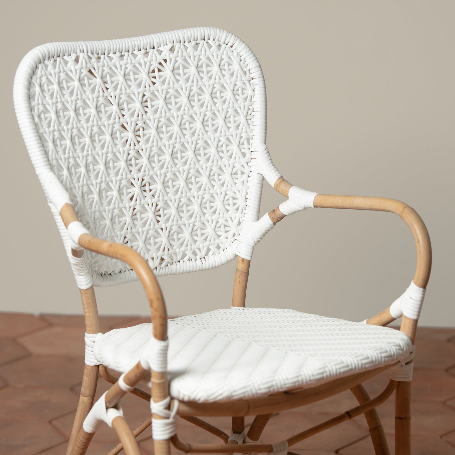 A close up of the neutral background is a white and tan woven rattan chair with woven cane on the backrest and seat.
