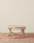 On a tan background is a round rattan coffee table with circle designs around the edge of the table.