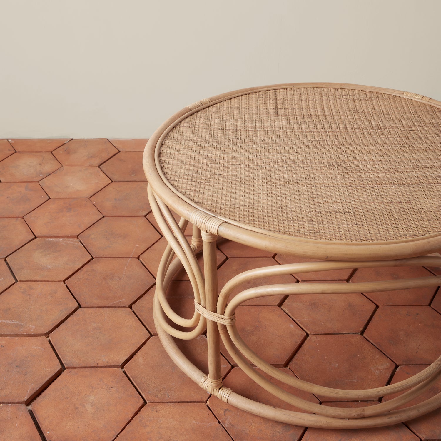 On a tan background is a round rattan coffee table with circle designs around the edge of the table.
