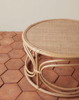 On a tan background is a round rattan coffee table with circle designs around the edge of the table.