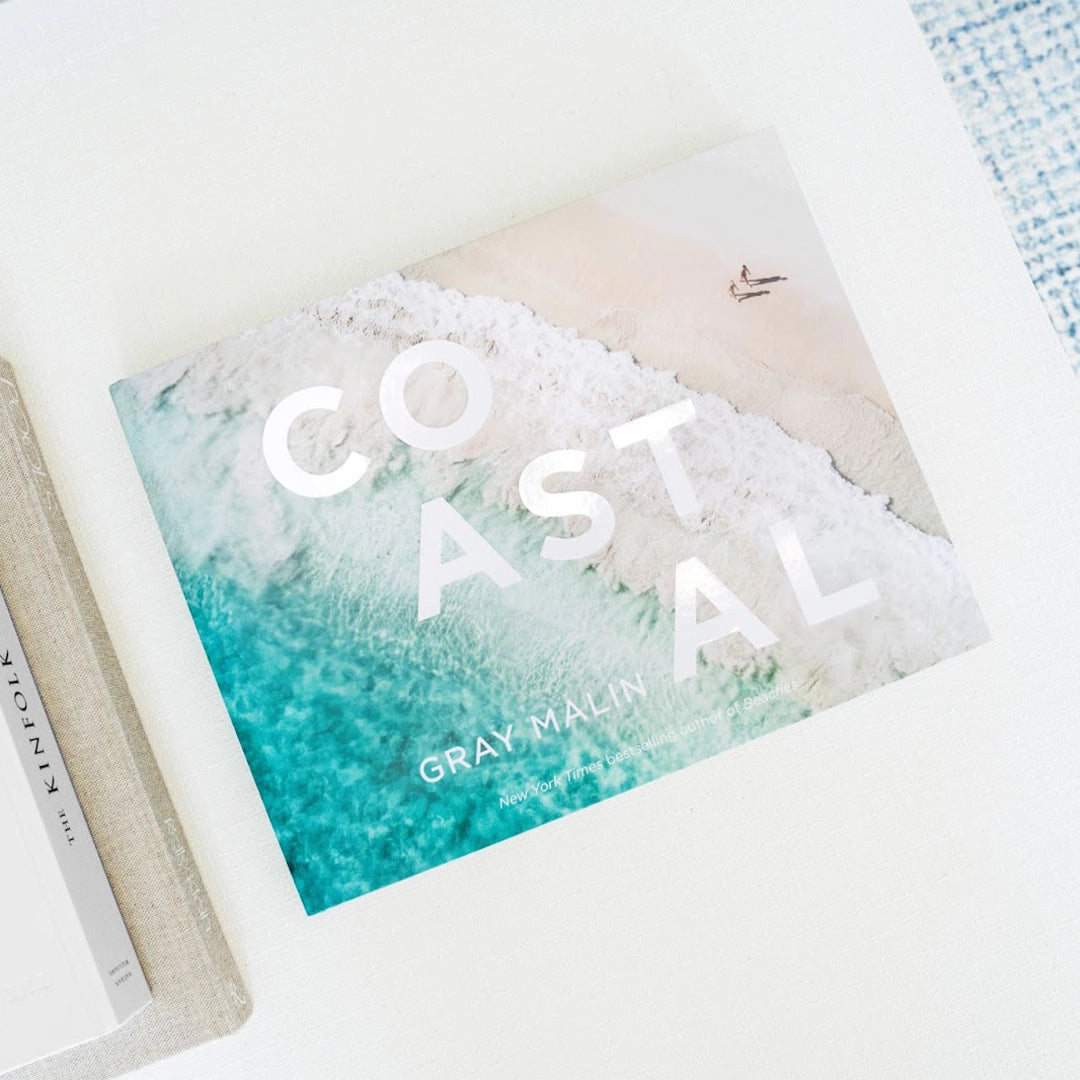 On a white background is a Gray Malin book cover with one of his ocean photography shots as well as white text that reads, &quot;COASTAL&quot;. 
