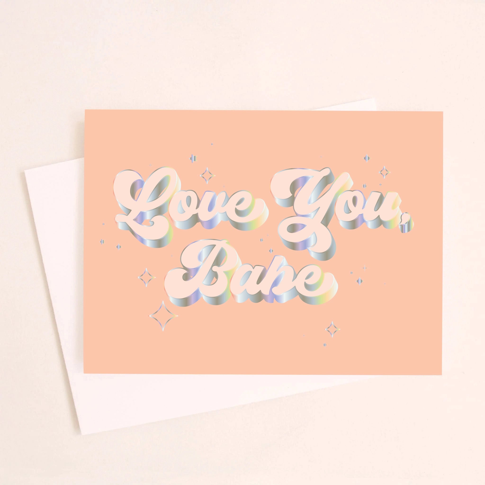 On a light peach background is a peachy greeting card with &quot;Love You Babe&quot; text in the center that is outlined with holographic foil detailing. Also included is a white envelope.