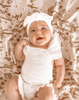 A baby laying on a light pink / neutral swaddle with a light brown palm and desert pattern swaddle.