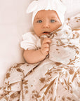 A baby laying on a light pink / neutral swaddle with a light brown palm and desert pattern swaddle.
