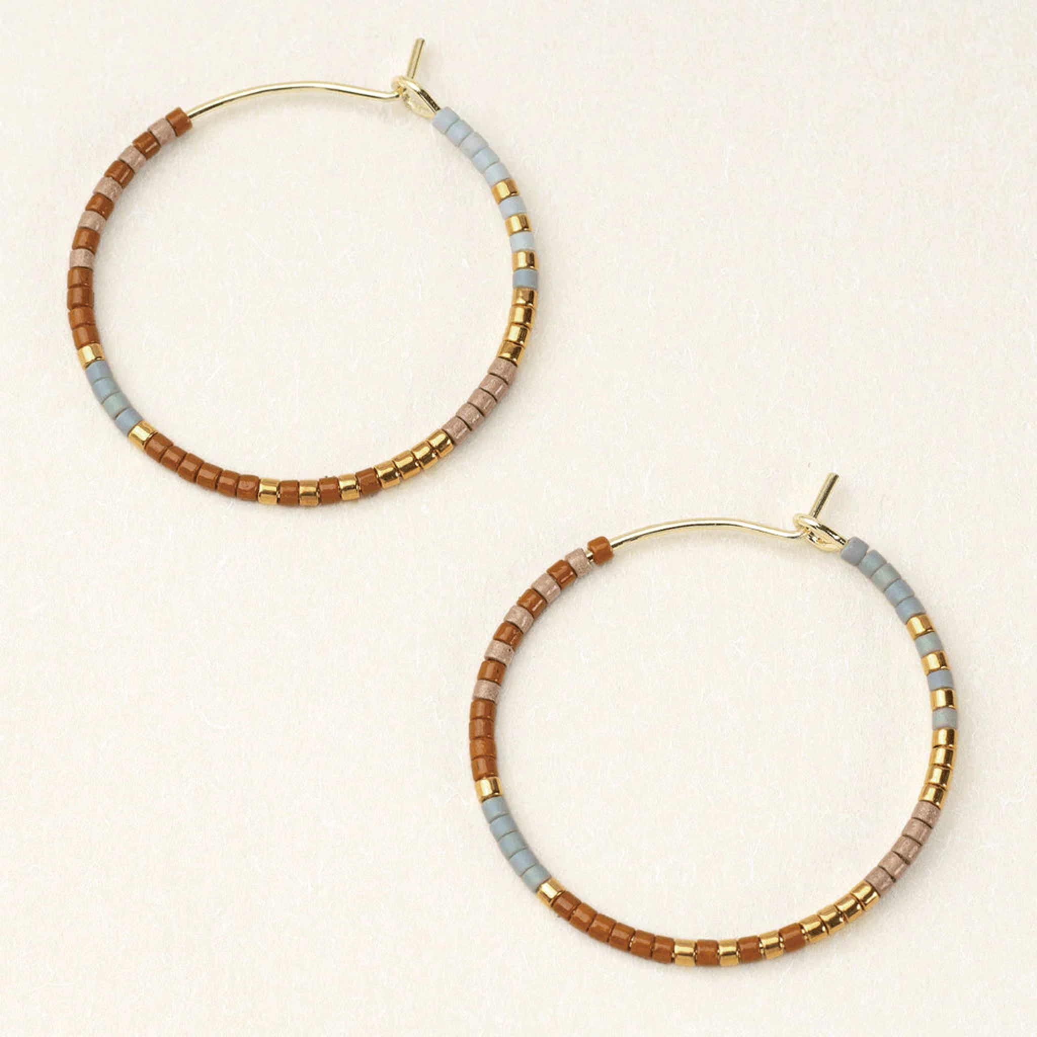 On an ivory background is a pair of gold hoops with multi-colored beads.