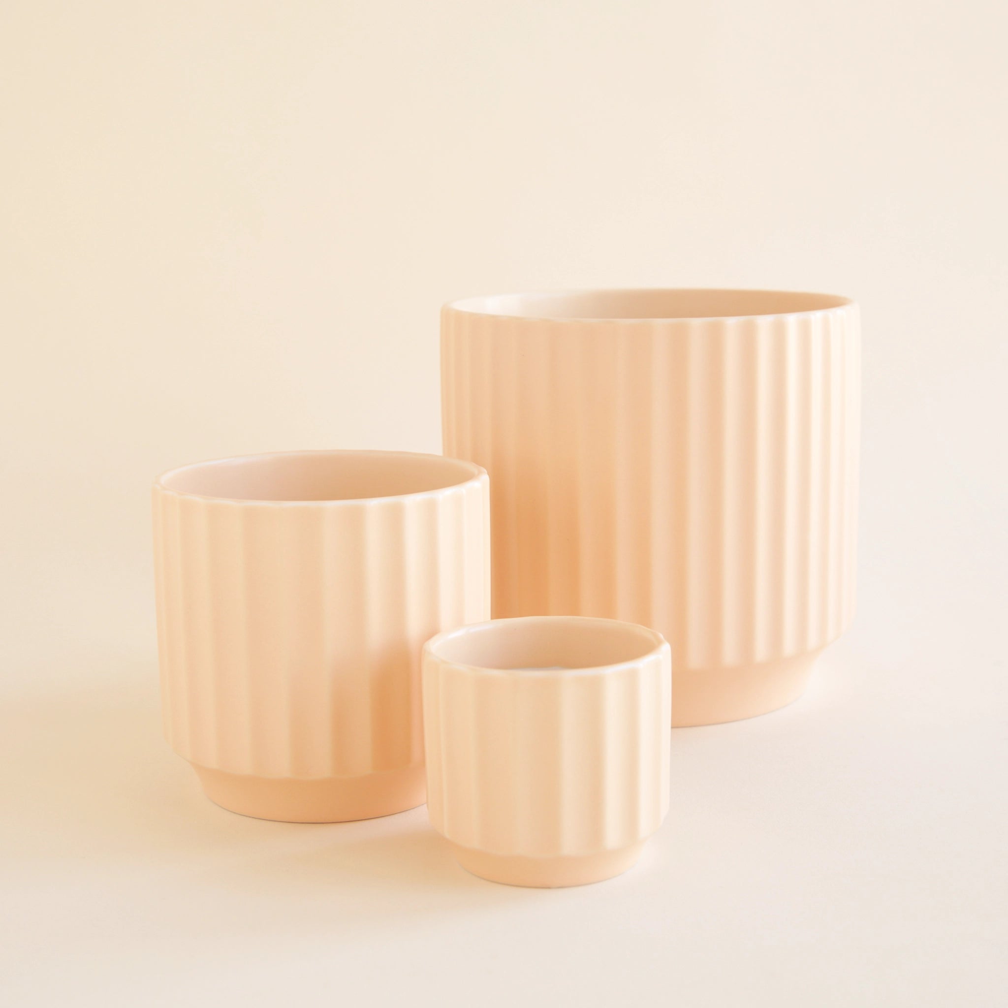 On a white background is three different sized ceramic pots with a fluted texture in a light pink shade.