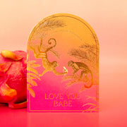 A pink and orange ombre arched shape card with gold foiled monkey illustrations and gold text that reads, "You Put The Ass In Potassium Love You Babe".