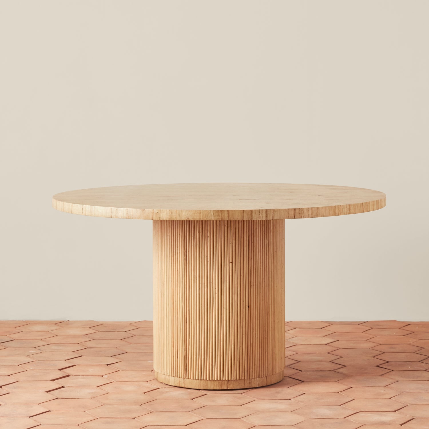 On a neutral background is a round wood table with a round fluted base.