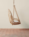 On a neutral background is a natural rattan egg shaped hanging chair with an ivory cushion and rope details.