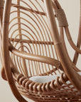 On a neutral background is a natural rattan egg shaped hanging chair with an ivory cushion and rope details.
