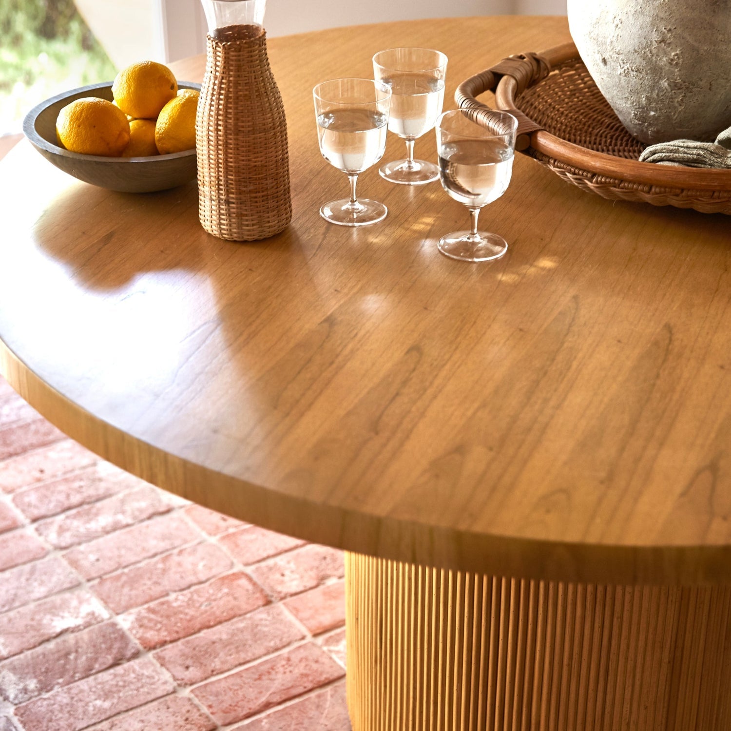 On a neutral background is a round wood table with a round fluted base.