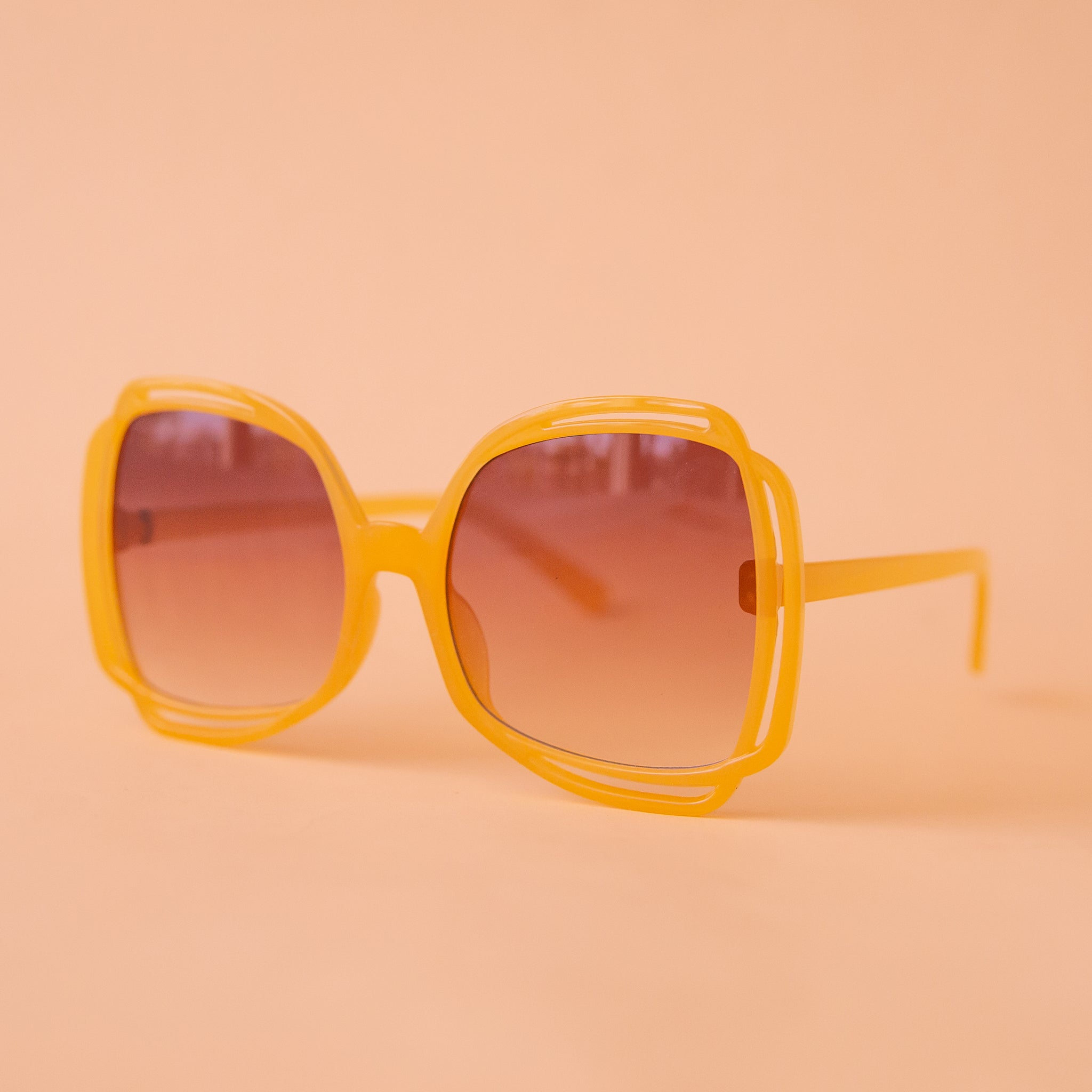A pair of round sunglasses with yellow frames and a brown gradient lenses.