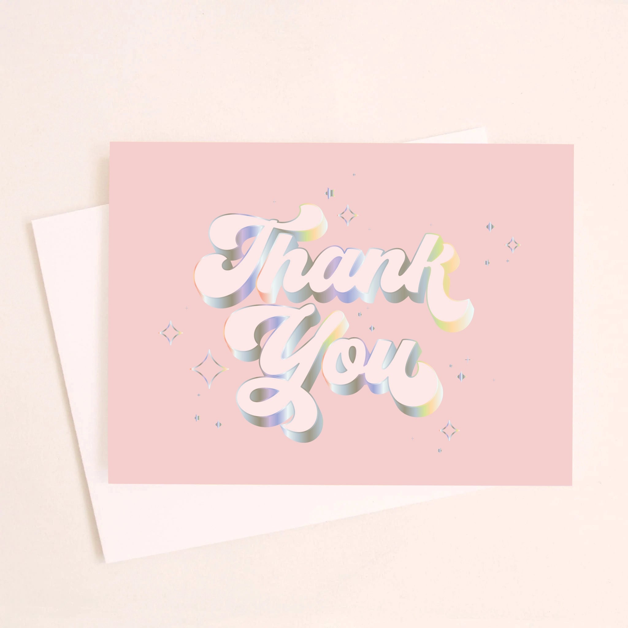 On an ivory background is a light pink card that reads, &quot;Thank You&quot; with in white text with holographic outlining.