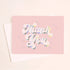 On an ivory background is a light pink card that reads, "Thank You" with in white text with holographic outlining.