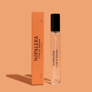 A travel bottle of perfume with a black lid, orange packaging and text that reads, 'Nopalera Flor De Madera'.