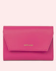 On a light pink background is a bright pink wallet with gold tiny text that reads, "Matt & Nat" on the front flap.